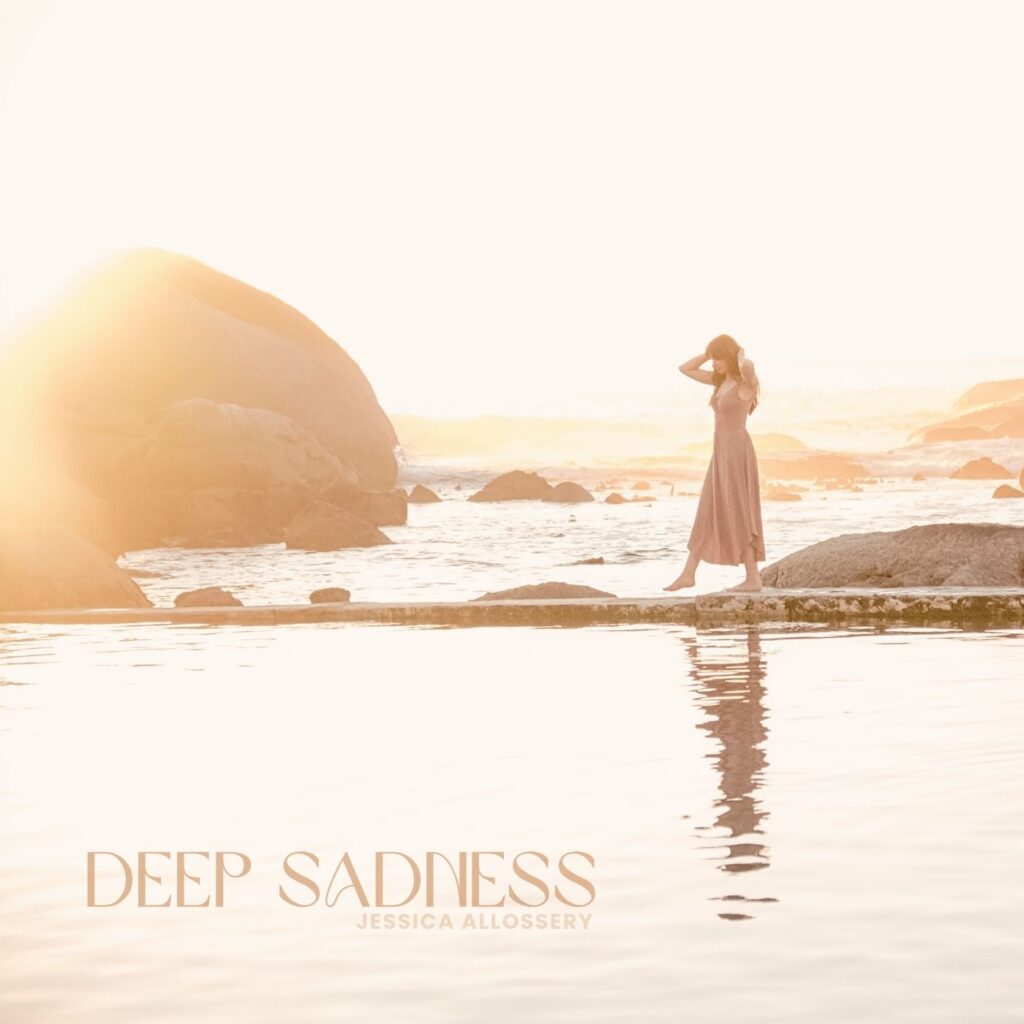 Girl on a beach with boulders in background at sunset, wearing flowy dress. Text Deep Sadness on the image and Jessica Allossery