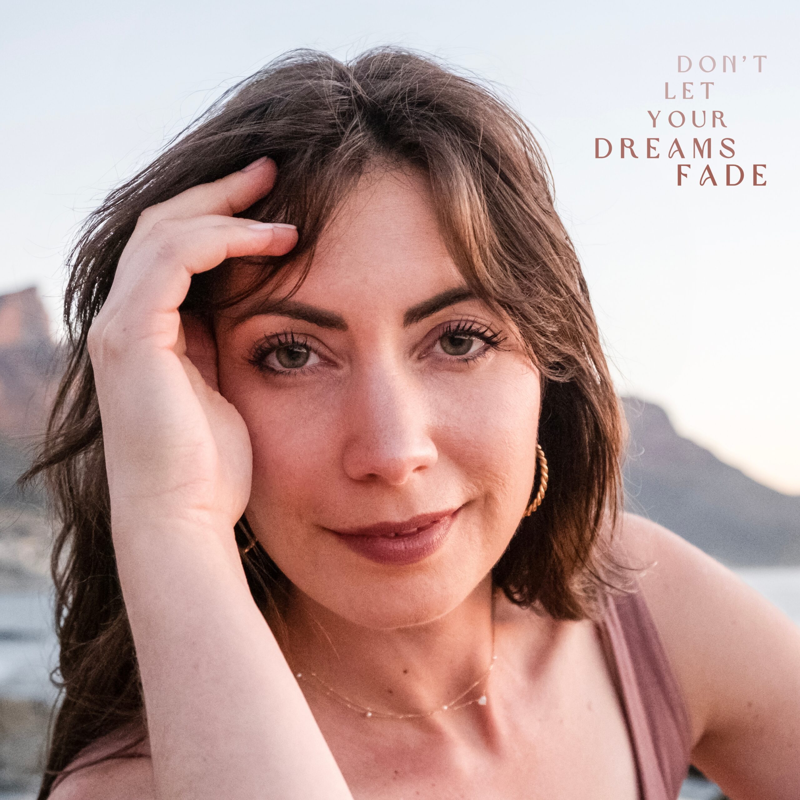woman on beach at sunset brushing hair away, half smiling