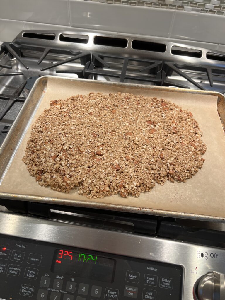 Raw Honey Almond granola spread on a lined baking sheet on top of the stove