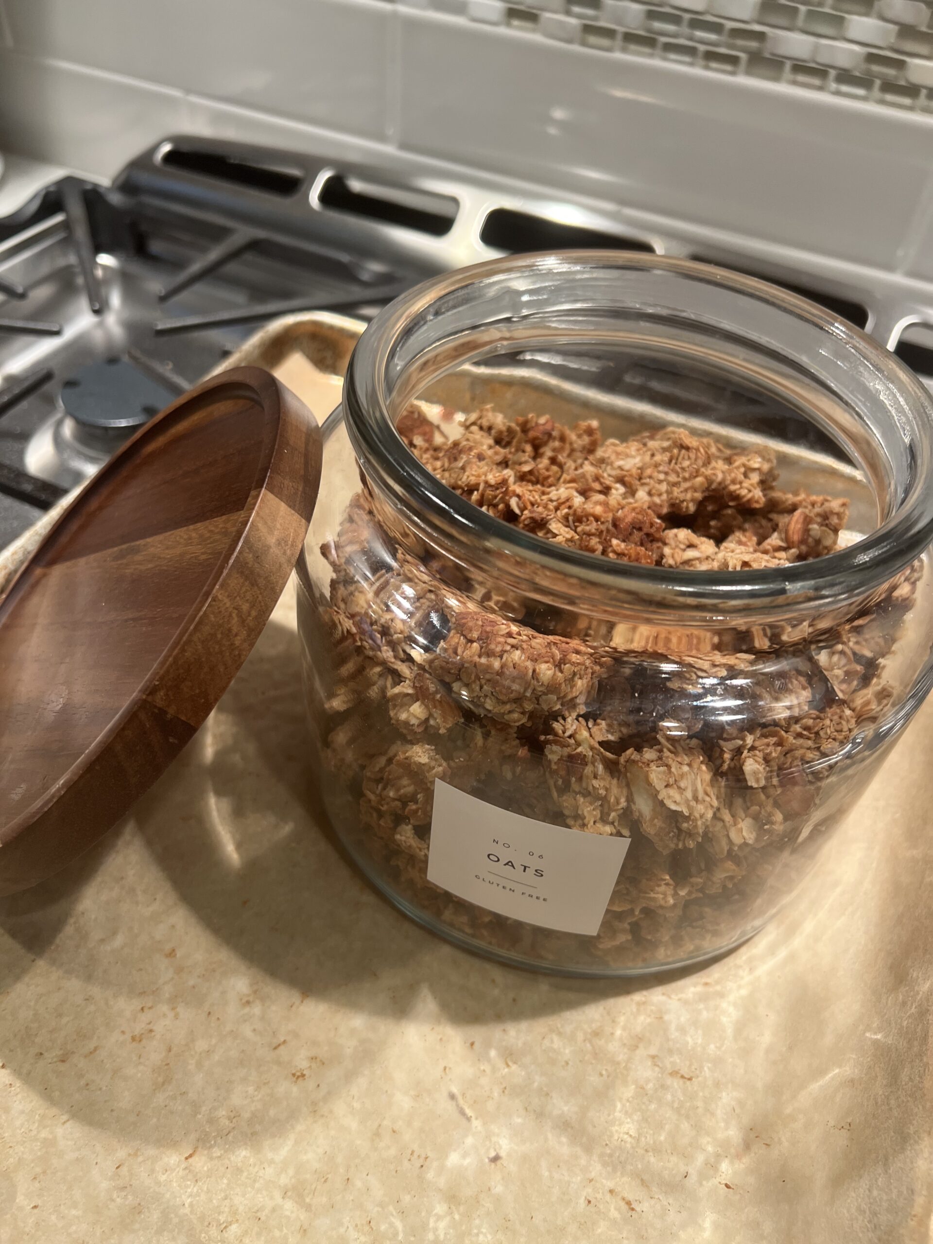 Almond granola in glass jar with wooden lid tilted on it's side on top of stove