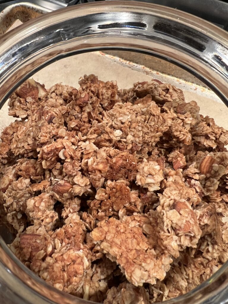 Close of chunks of honey almond granola in a glass jar on top of the stove