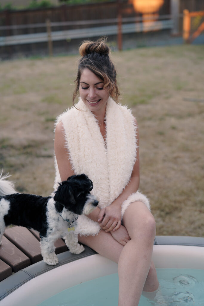 Woman with black and white biewer terrier sitting at edge of blow up hot tub in yard.