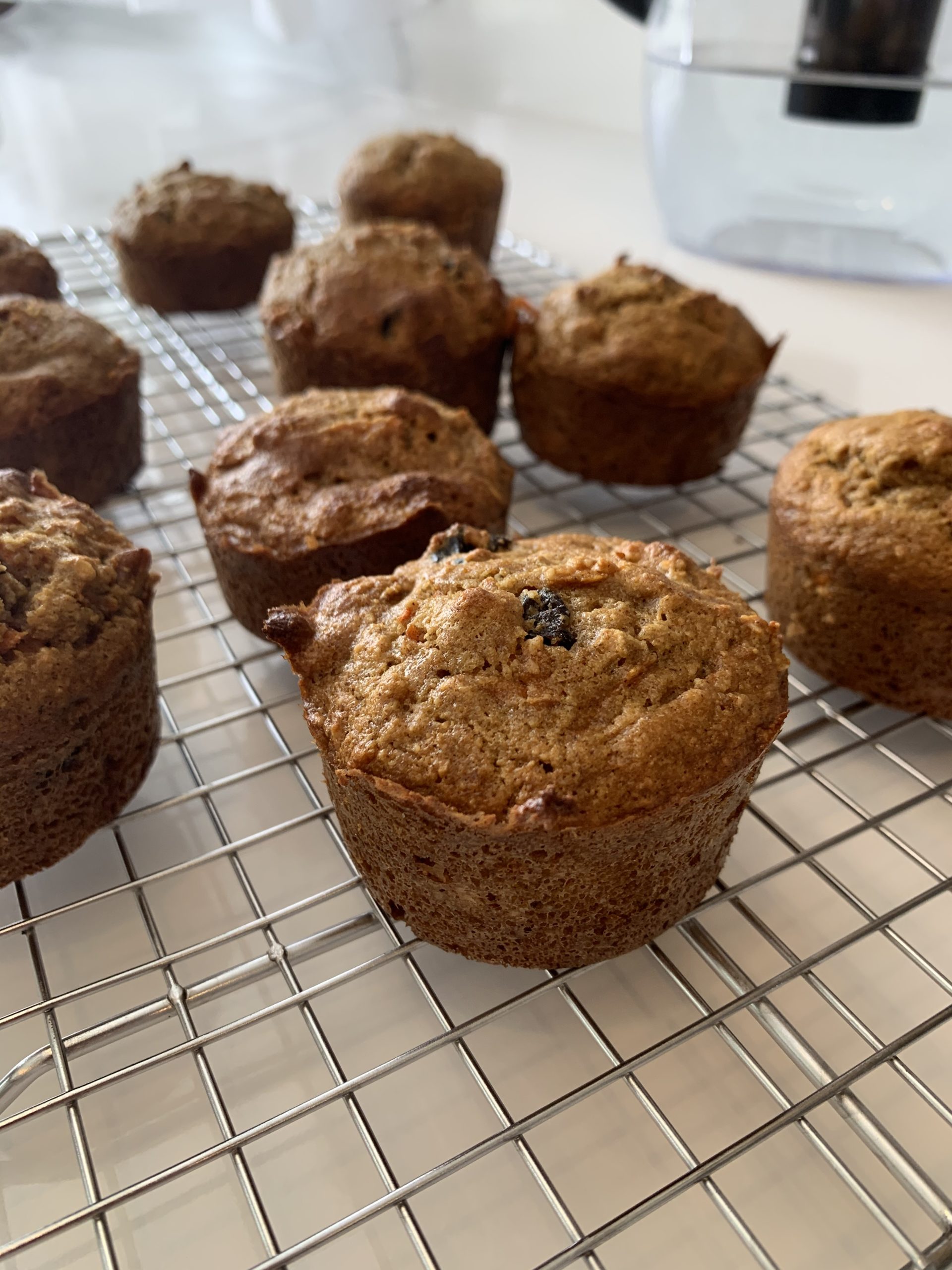 Many spiced carrot-raisin muffins cooling on a cooling rack in a kitchen.